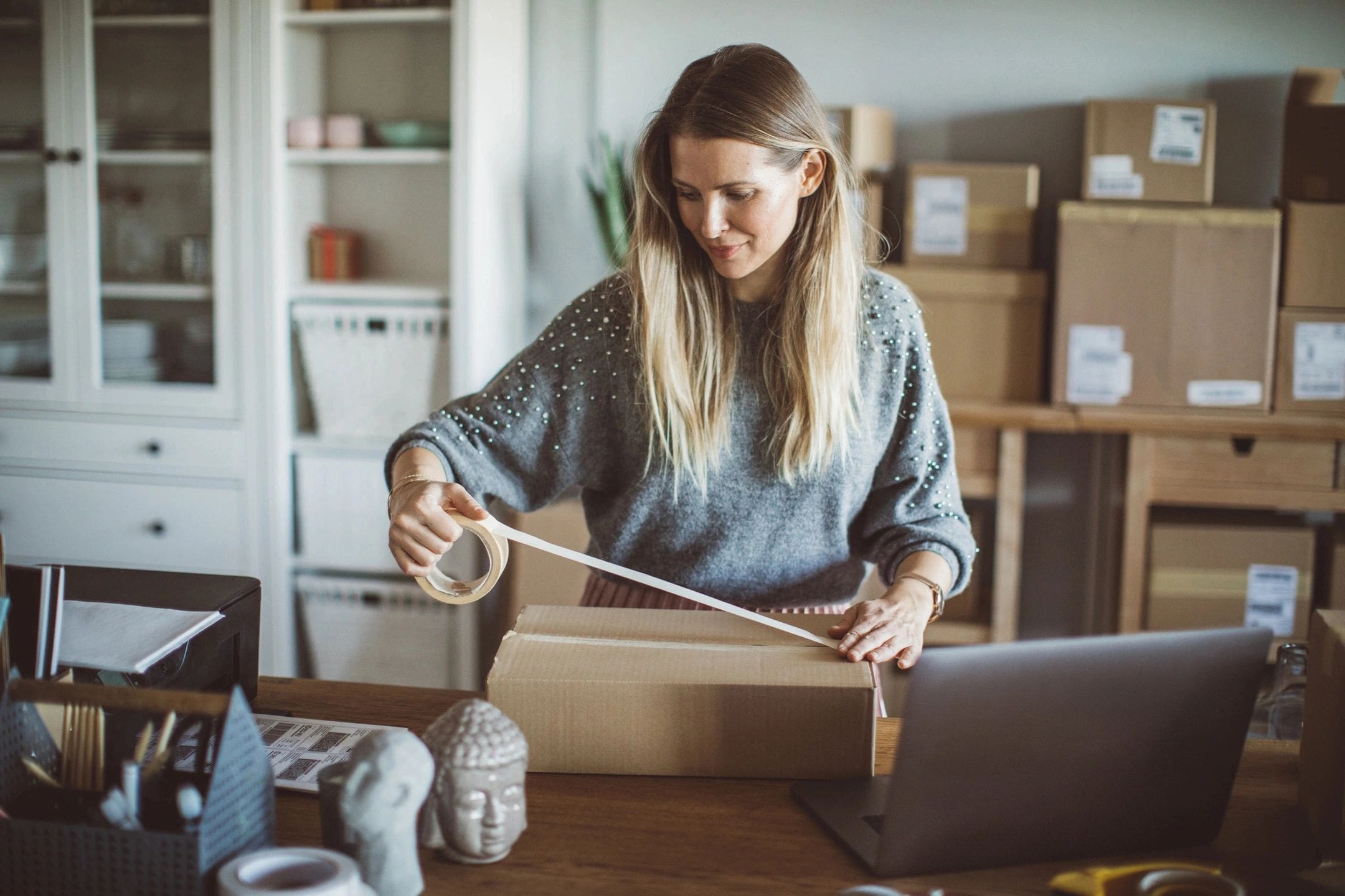 A woman is cutting tape off of a box.